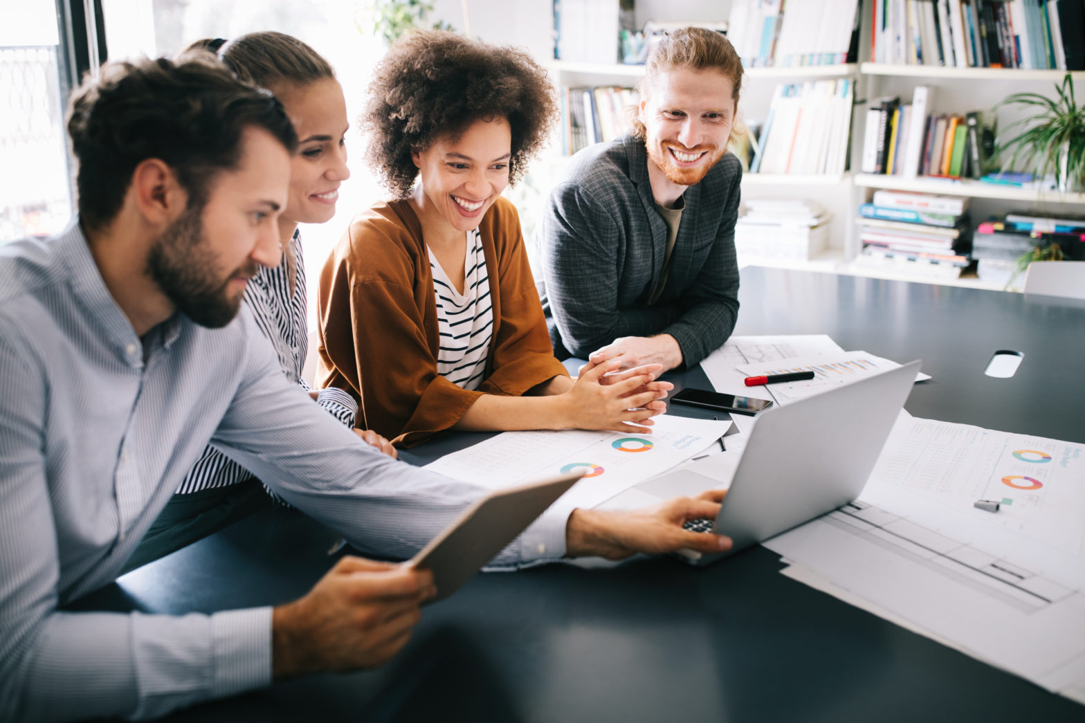 Group of four coworkers looking at a laptop and tablet discussing ERP options