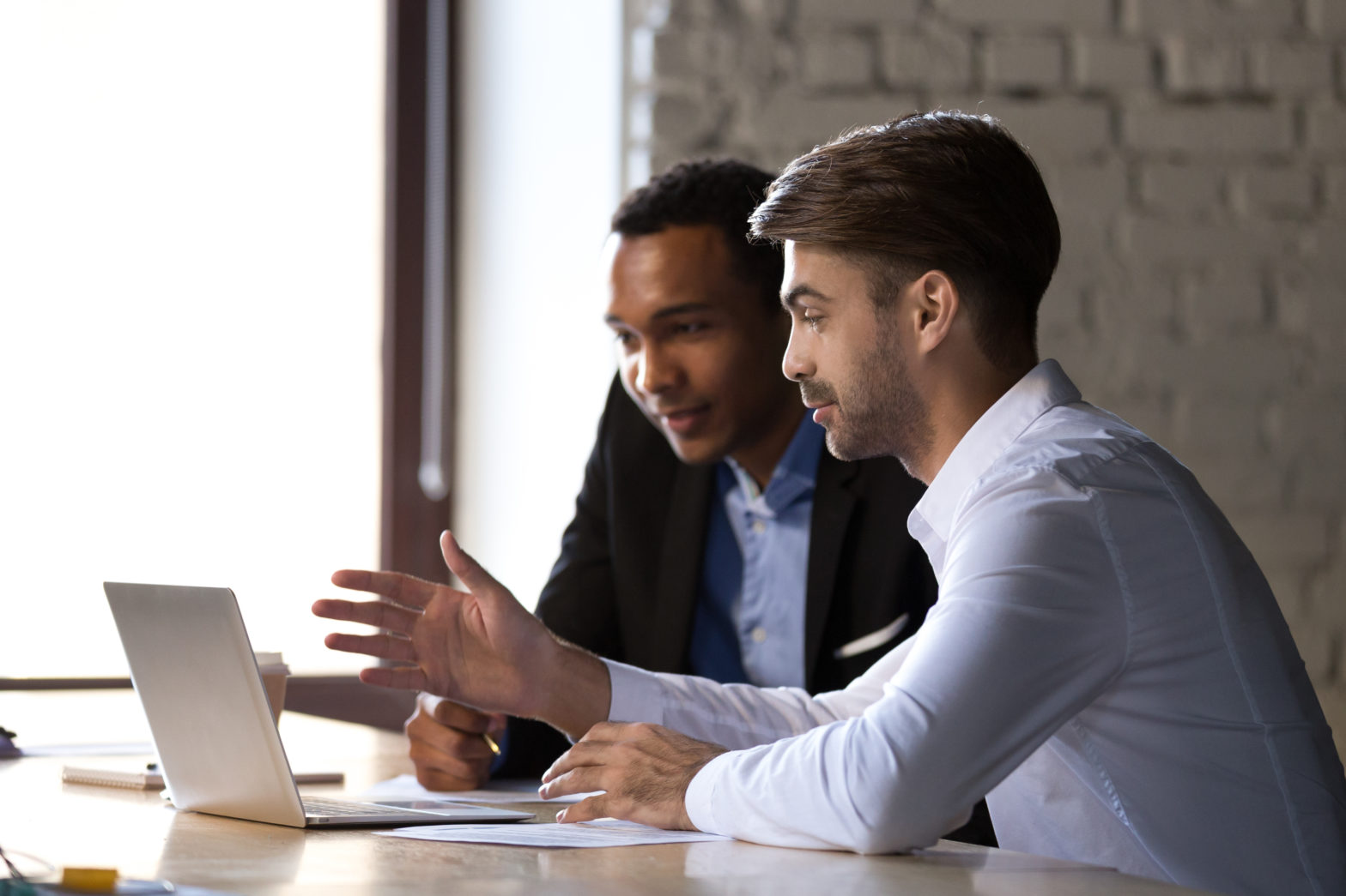 Two male coworkers having a discussion on their laptop