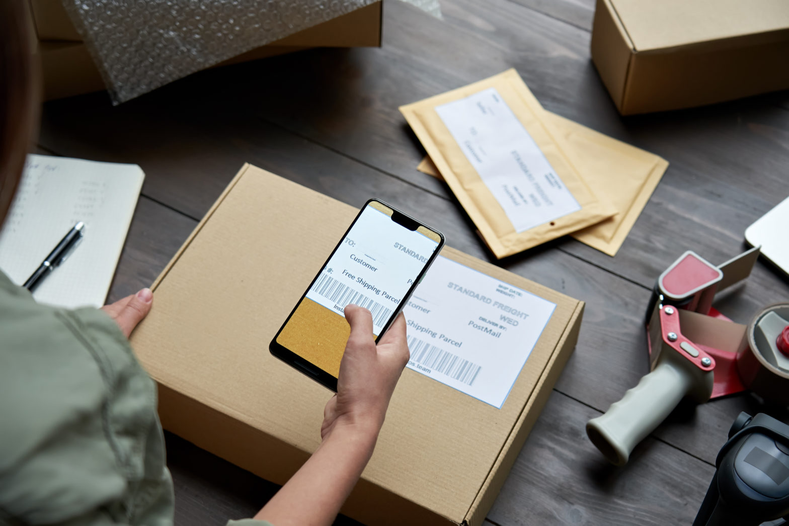 Woman boxing up a shipment and scanning the barcode with her mobile device