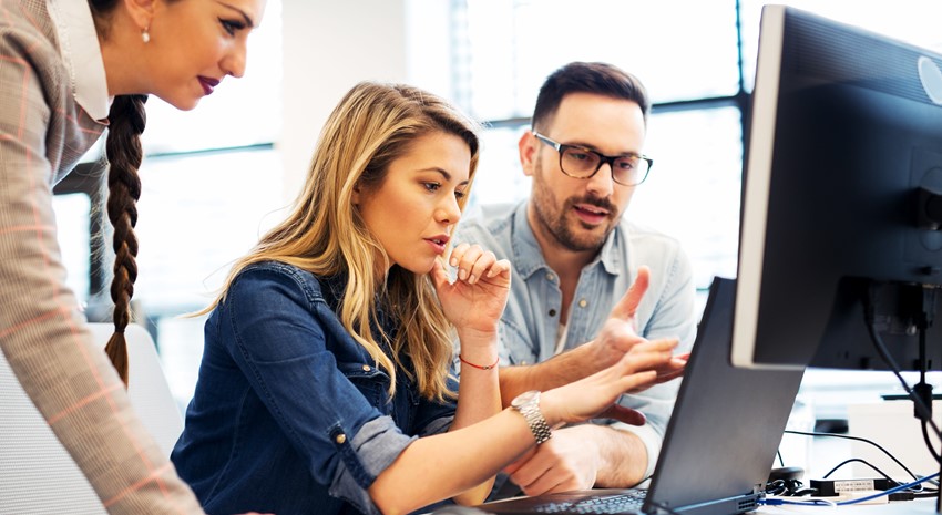 Three coworkers looking at a laptop together