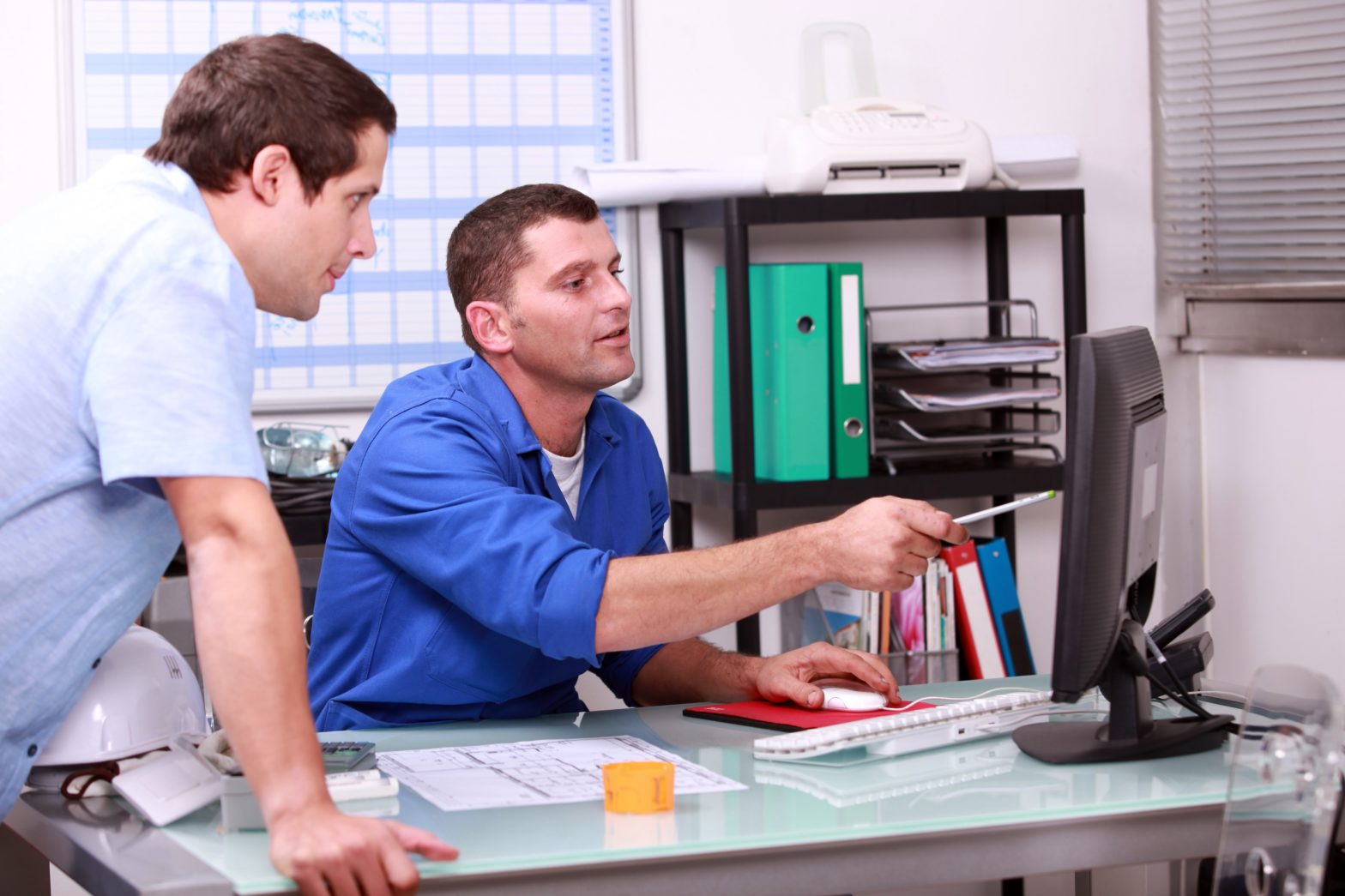 Two male coworkers looking at their ERP software on the computer and having a discussion