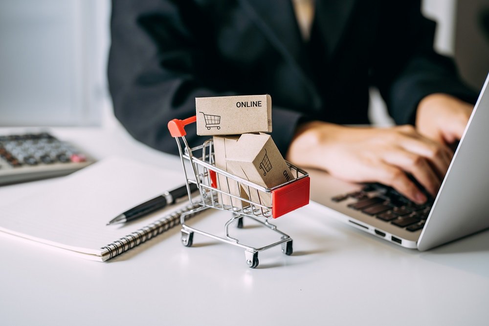 Woman typing on laptop with mini shopping cart with boxes on her desk