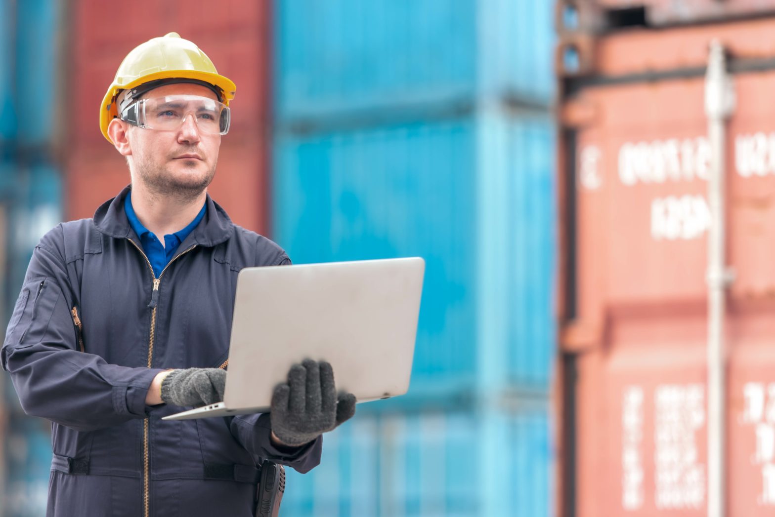 Distributer employee outside near shipping containers holding a open laptop