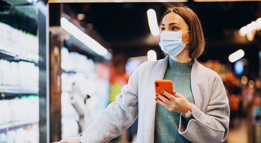 Woman grocery shopping with face mask and holding a cell phone