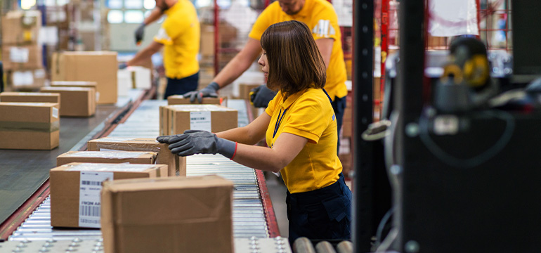 Multiple employees working to sort through boxes on a moving line, focusing on a female looking at a box