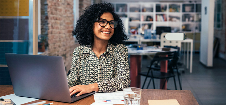 Female business professional in a casual setting smiling while on her laptop working