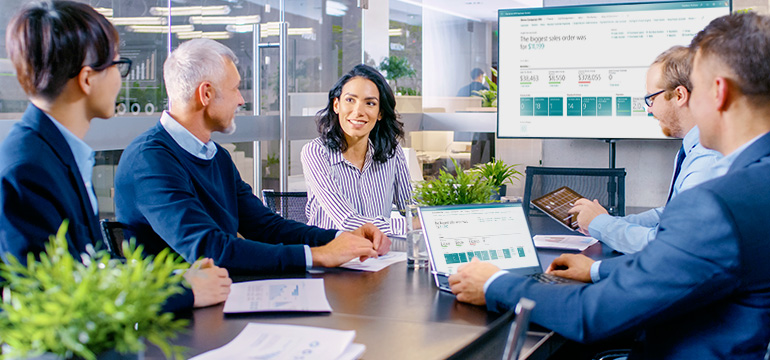 Consulting professionals in a boardroom talking and sharing the Dynamics 365 Business Central dashboard on multiple screens and devices