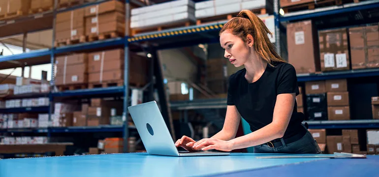 A woman types on a laptop in a warehouse